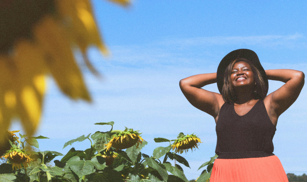 Embracing Spring: How More Sunlight Can Boost Your Mental Health. Image of a woman standing out in a sunny sunflower field.