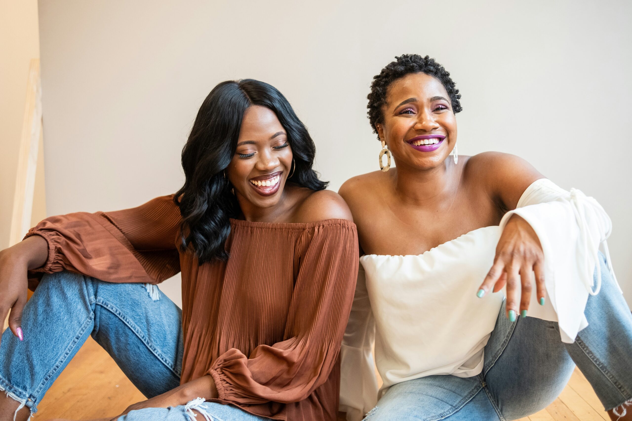 Friendship 101: How to Keep Your Girl Gang Thriving. Image of two women sitting on the floor and smiling together. Friendships.