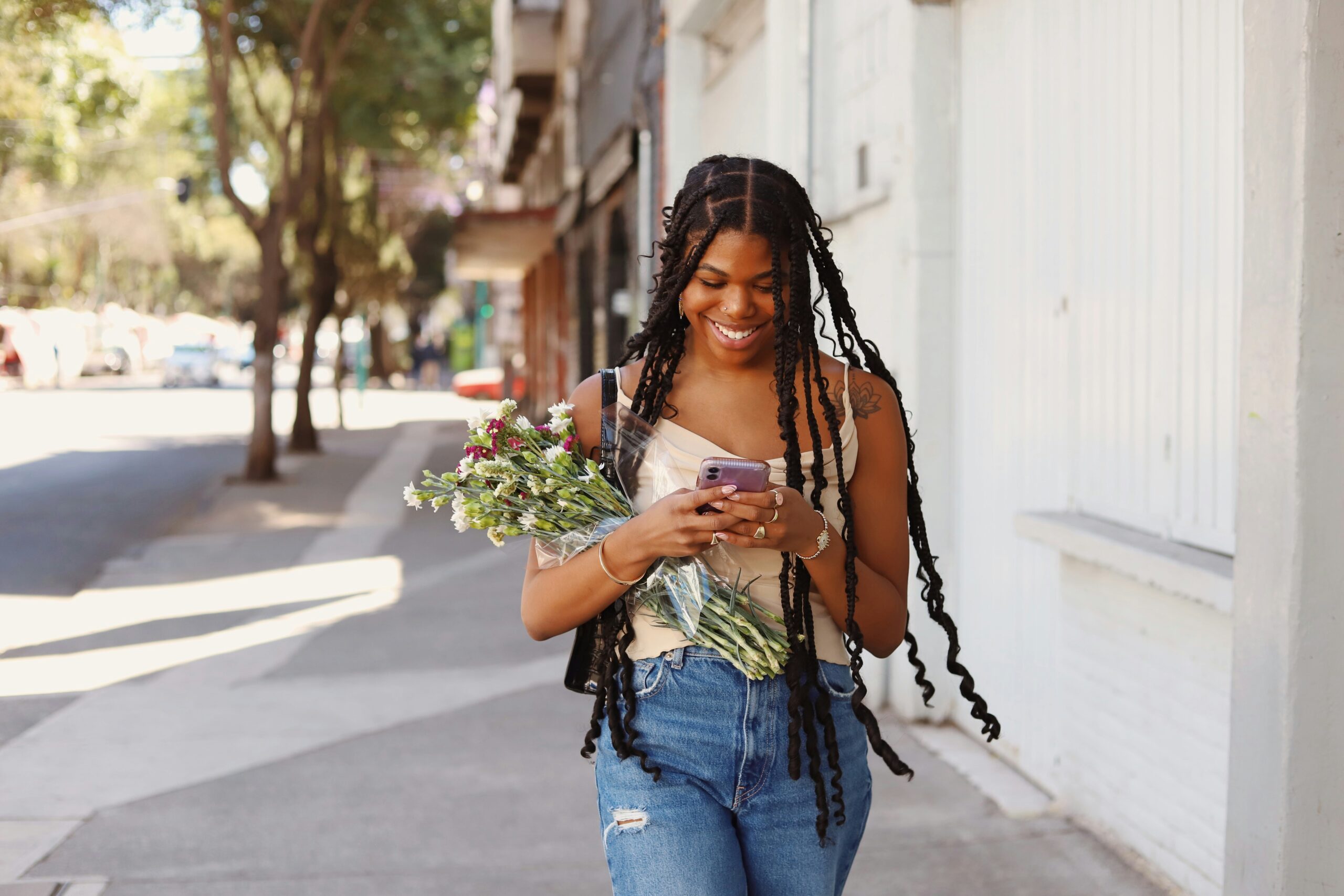 Debunking Mental Health Myths. Image of a woman smiling while walking down a sidewalk, looking at her phone, holding a bouquet of flowers.