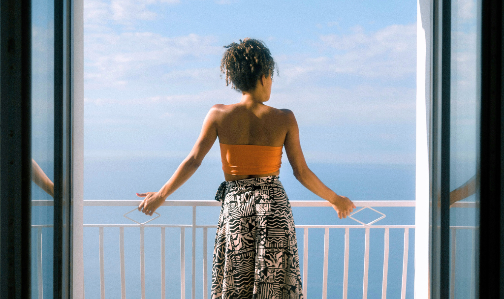 Vacation and Mental Health. Image of a woman standing on a balcony overlooking an ocean.